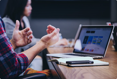 Trust Patrick's member is gesturing while consulting at a table with a laptop open, displaying colorful graphs. Another person is blurred in the background, creating an engaged, professional atmosphere.