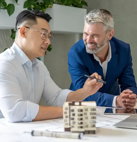 Two men discuss architectural plans at a desk with a building model.