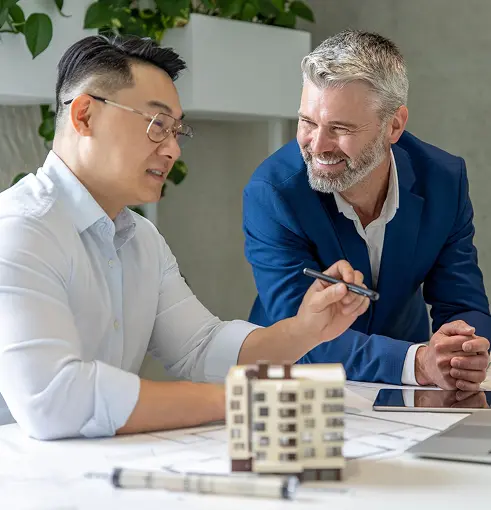 Two men discuss architectural plans at a desk with a building model.